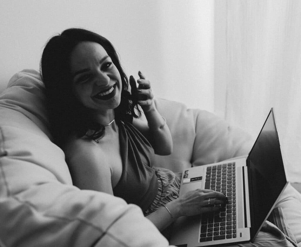 Traurednerin Helene Bauer lacht entspannt im Sitzsack während sie am Laptop an einer Hochzeitsrede arbeitet (Schwarz-Weiß)