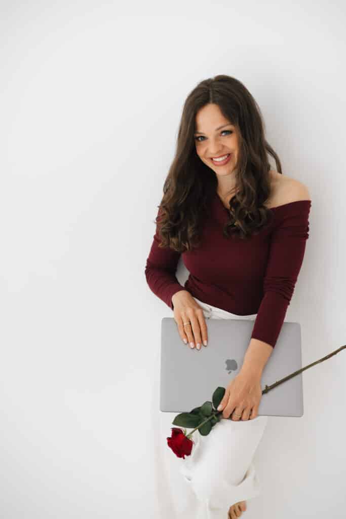Traurednerin Helene Bauer lächelt mit einem Laptop und einer roten Rose in der Hand.